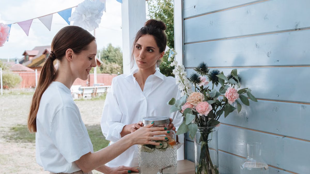Two women enjoying a summer garden party with lemonade and floral decorations.